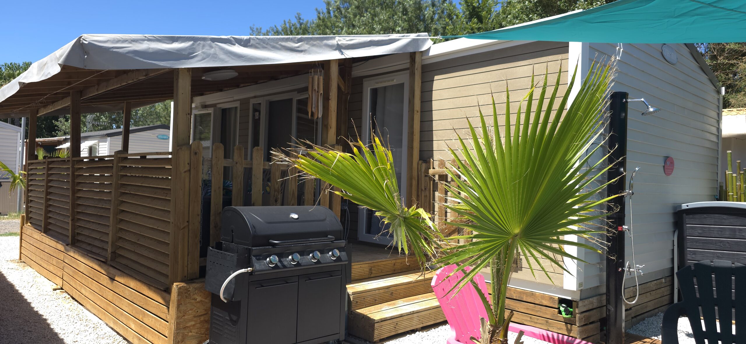 Le mobil-home et sa terrasse couverte, avec la plancha et les palmiers